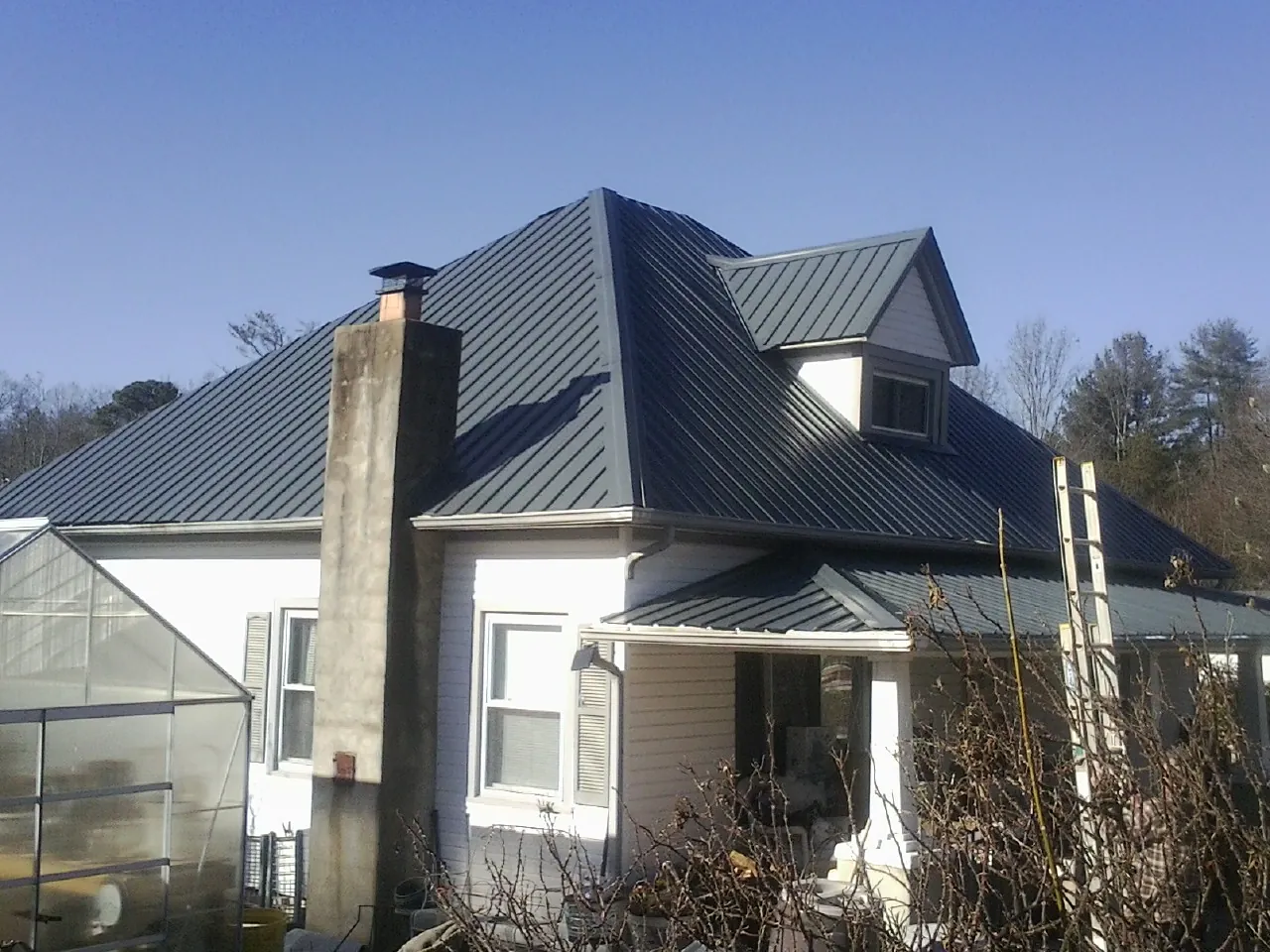 Dark blue standing seam metal roof on a white farmhouse with dormer — Slate & Tile Roof Repair by Roofing Brothers in Pierpont