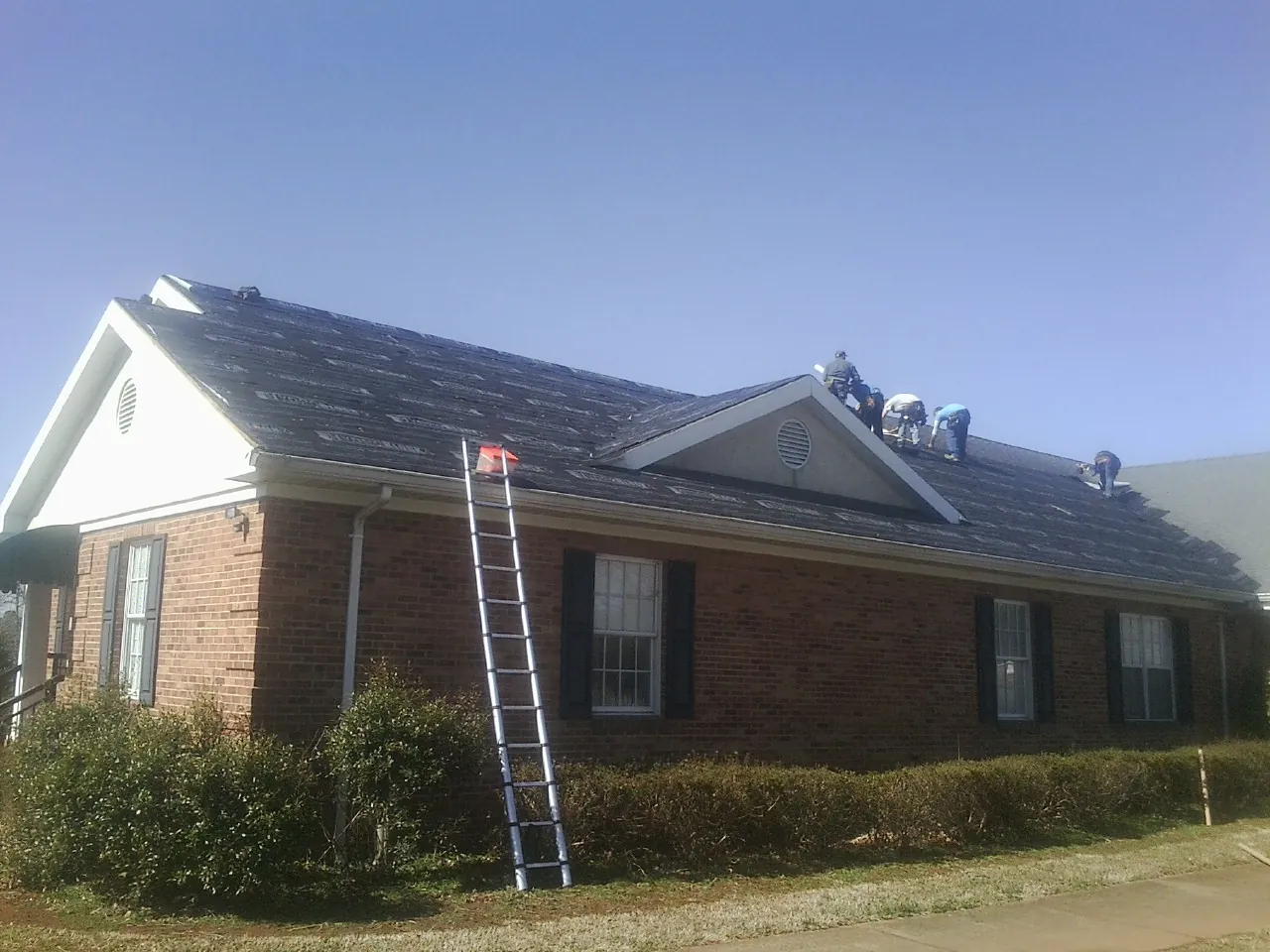 Crew tearing shingles off a brick ranch roof with a ladder set — Emergency Roof Repair work by our crew in Pierpont