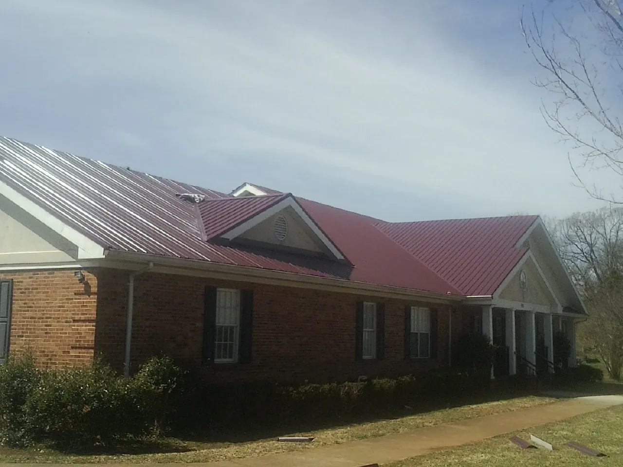 Red metal roof with gabled entries on a long brick building, from a Hail Damage Roof Repair job in Pierpont