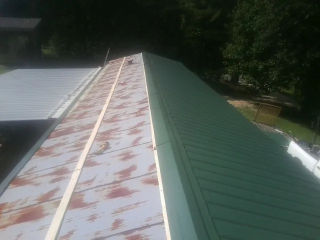 Old rusted panels beside newly installed green metal roofing — Wind Damage Roof Repair by Roofing Brothers in Pierpont