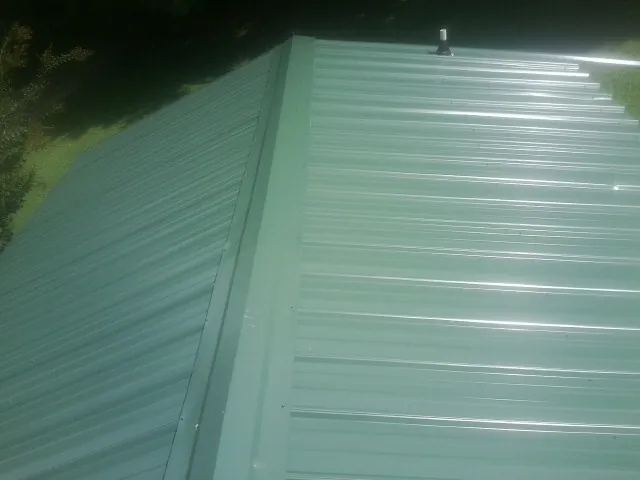 New green metal panels meeting at the ridge of a roof — Flat Roof Repair work by our crew in Pierpont