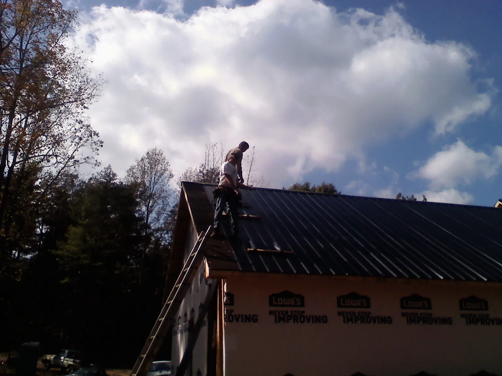 Roofer fastening dark metal panels high against a cloudy sky, from a Roof Inspection job in Pierpont