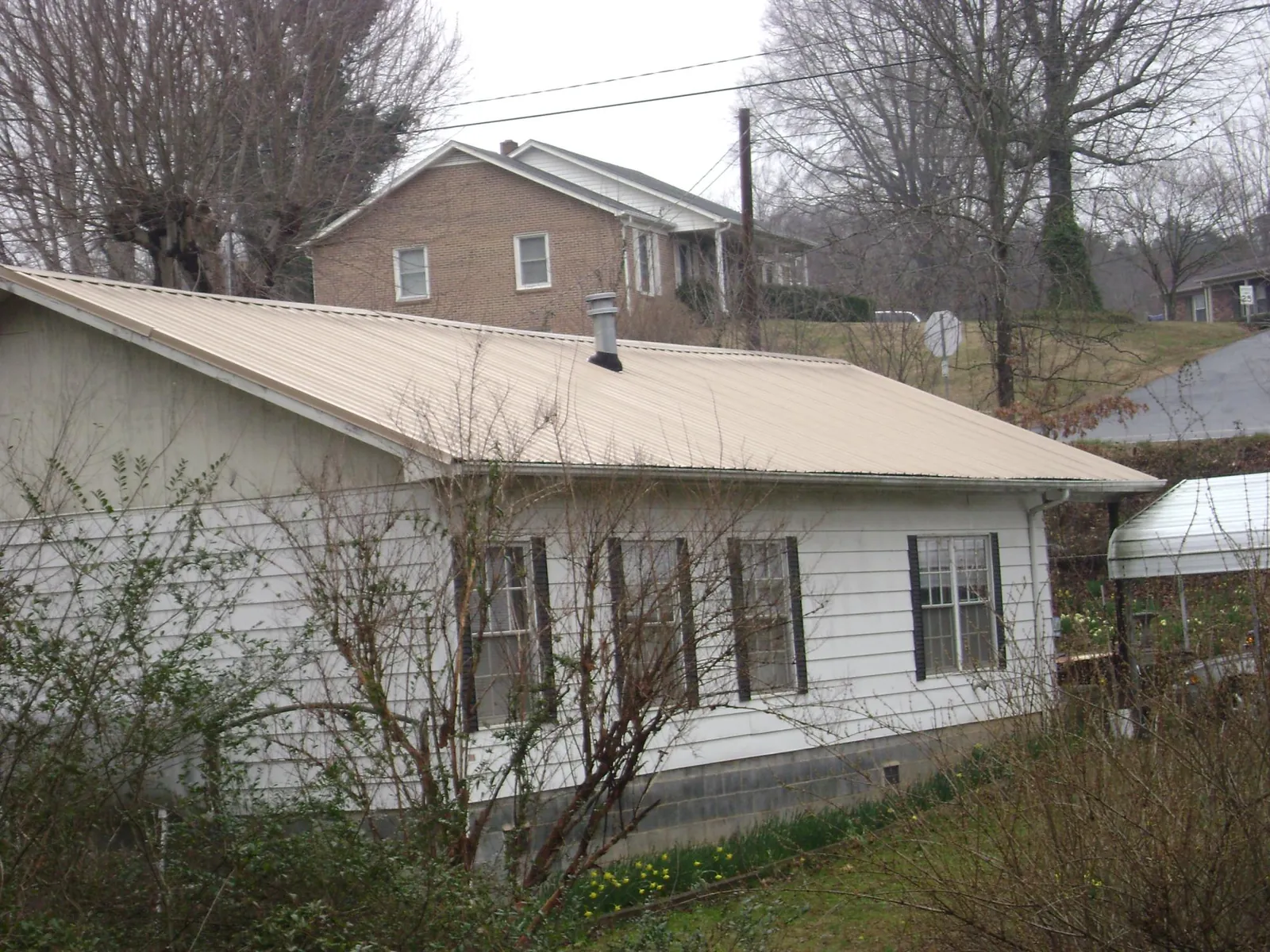 Tan metal roof on a white sided house set into a hillside — Commercial Roofing by Roofing Brothers in Pierpont