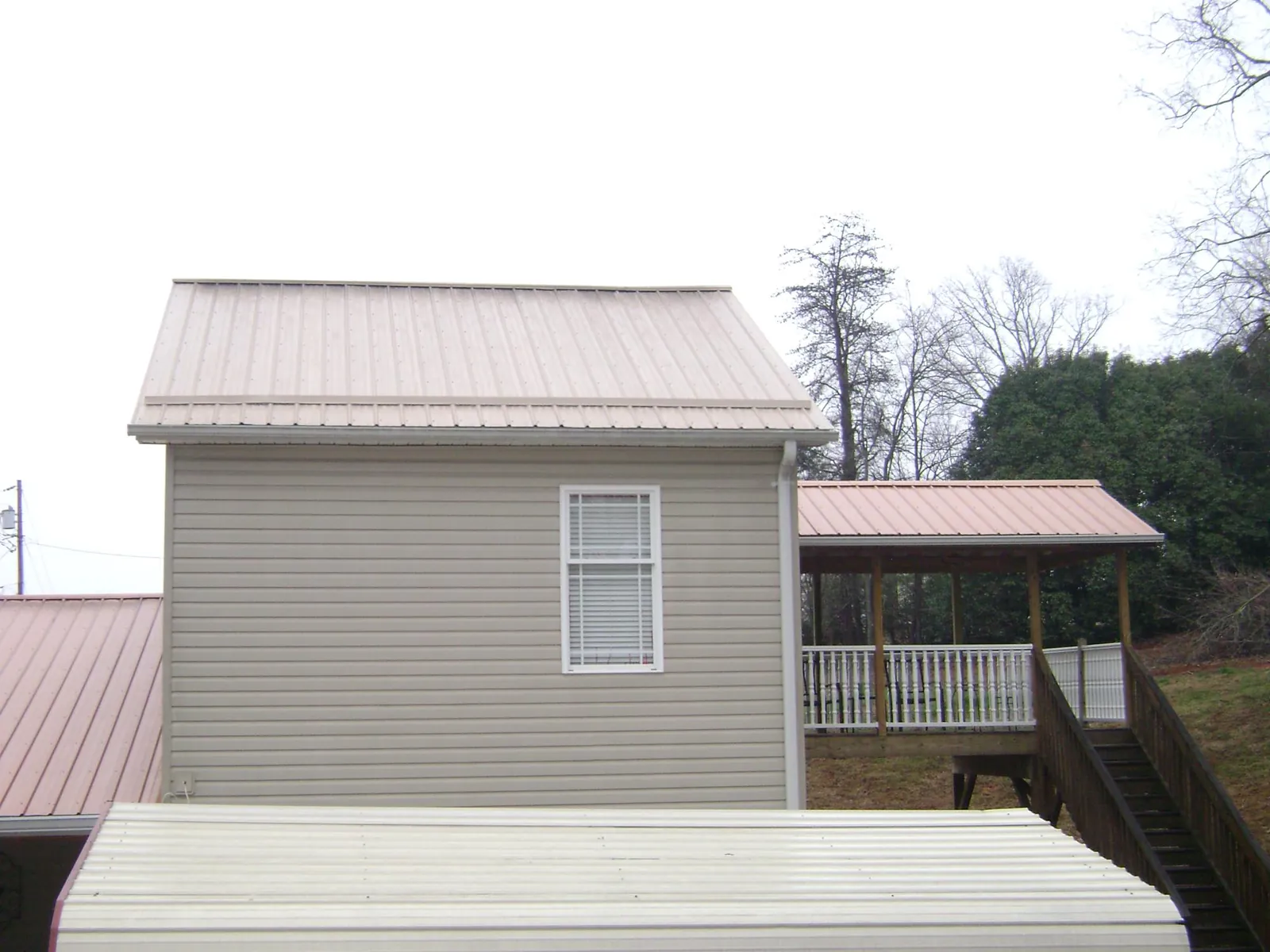Tan metal roofs on a two story addition and attached porch, from a Roof Replacement job in Pierpont